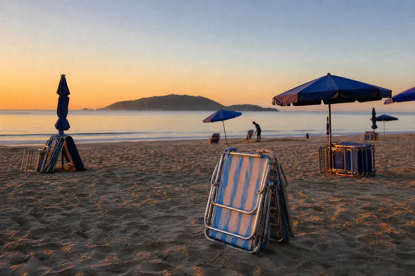Guarda-sóis e cadeiras de praia sendo organizados na areia ao amanhecer